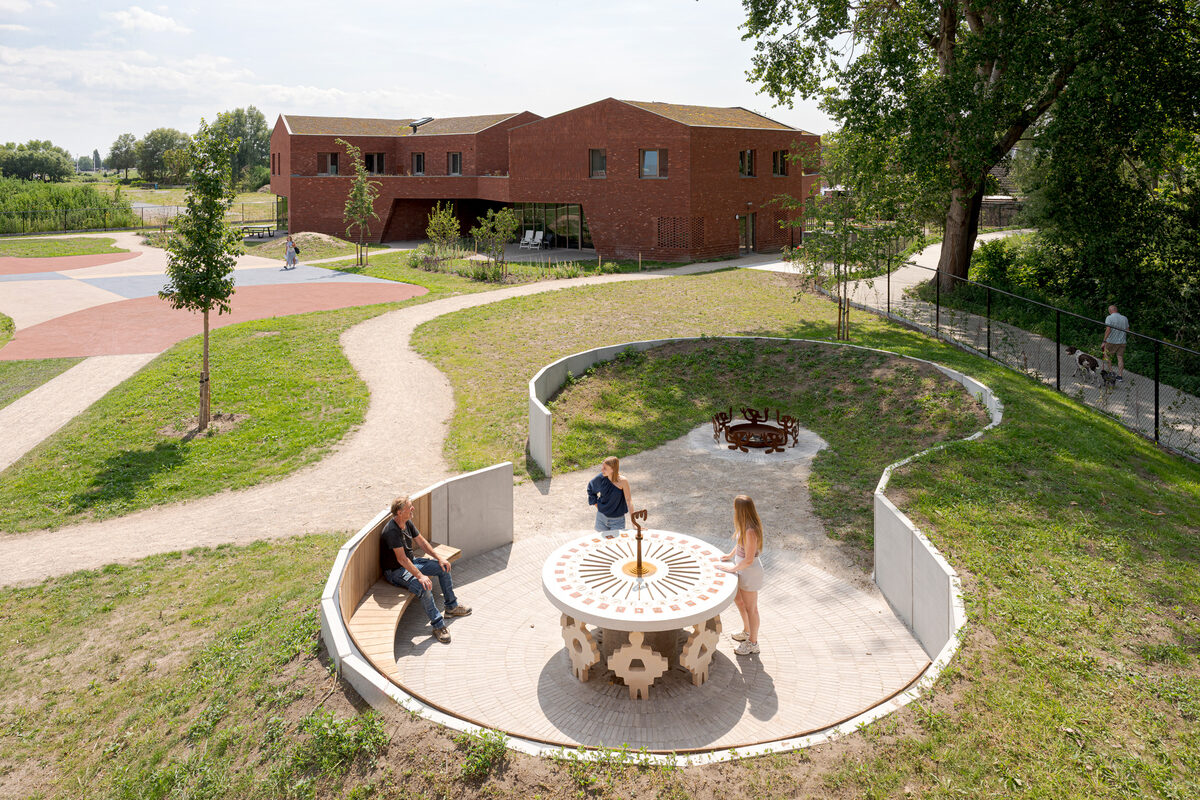 Frank&Robbert Robbert&Frank, *[Mandorla](\artworks\c8c03b4d-0e55-4632-901c-08de8728affe)* (2024 - 2025). View from the South Building of the site-specific installation at ARCADE Group, Gistel, Belgium: a circular concrete structure set within the garden, with metal guardian figures surrounding a fire pit and a central table bearing over sixty ceramic amulets arranged around a sundial.